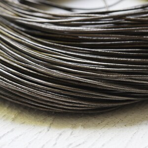 May include: Close-up of a reel of dark brown leather cord. The cord is smooth and supple, and it is wound tightly around the reel.