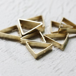 May include: A group of small, gold-coloured triangle-shaped metal charms with holes in the corners. The charms are arranged in a pile on a white surface.