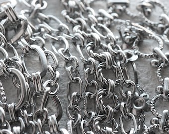 May include: A close-up of a pile of silver chains of different styles and sizes. The chains are intertwined and create a textured, metallic background.