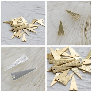 May include: A pile of gold-colored triangle-shaped metal charms with a sparkly finish. The charms have two holes at the top.
