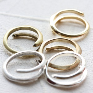 May include: Five gold and silver rings, some with a twisted design, are arranged on a white surface.