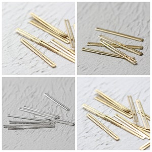 May include: A collection of gold and silver metal bar shapes with a hollow centre. The bars are arranged in a pile on a white surface.