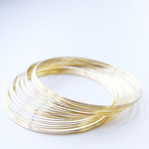 Puede incluir: Una pila de anillos finos de metal de color dorado, apilados uno encima del otro. Los anillos son todos del mismo tamaño y están dispuestos en un patrón circular.