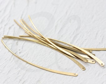 May include: A collection of slender, curved, gold-colored metal bars, each with a small hole at one end. The bars are scattered on a white surface, suggesting a craft or jewelry-making theme. The overall aesthetic is minimalist and elegant.