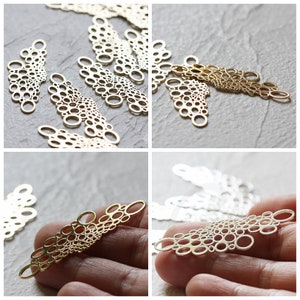May include: A set of gold-colored metal charms shaped like a cluster of circles. The charms are arranged in a fan shape and have a delicate, intricate design.