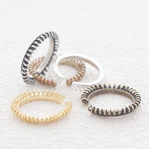 May include: Five adjustable rings with different finishes. The rings are made of metal and have a textured, coiled design. The rings are in various colors, including gold, silver, and black.