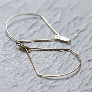 May include: A pair of gold-toned geometric hoop earrings. The earrings are shaped like teardrops with a slightly curved top.