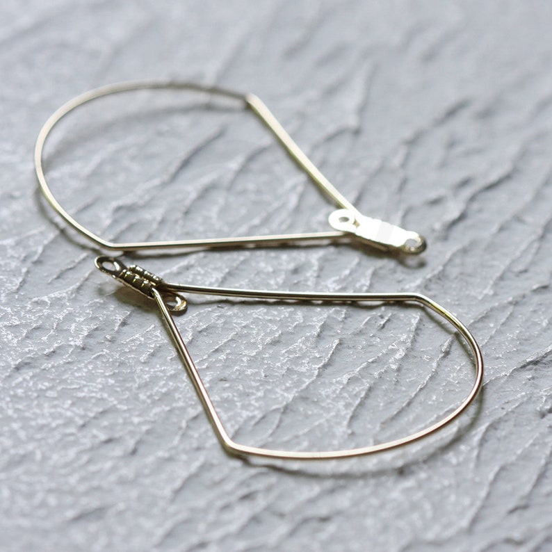 May include: A pair of gold-toned geometric hoop earrings. The earrings are shaped like teardrops with a slightly curved top.