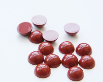 May include: A collection of 14 red gemstone cabochons, each with a smooth, rounded surface. The cabochons are arranged in a loose cluster on a white background.