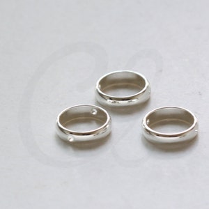 May include: Three silver rings, each with a hole. The rings are smooth and shiny.