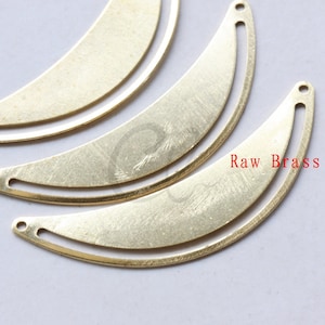 May include: Three raw brass crescent moon shapes with a hole at each end. The crescent moon shapes are stacked on top of each other. The text "Raw Brass" is visible in the bottom right corner of the image.