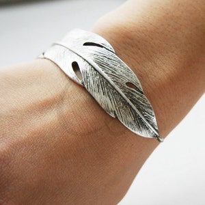 May include: A silver feather cuff bracelet. The bracelet is made of metal and has a detailed feather design.