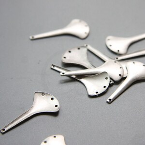 Puede incluir: Un grupo de piezas de metal plateado en forma de abanico con agujeros. Las piezas est&aacute;n esparcidas sobre una superficie gris.