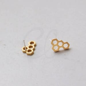 May include: A pair of gold-toned honeycomb-shaped stud earrings. The earrings are made of metal and have a simple, geometric design.