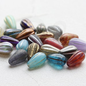 Op de afbeelding: Assortiment van kleurrijke glazen kralen in verschillende vormen en maten. De kralen zijn traanvormig en hebben een getextureerd oppervlak. Sommige kralen hebben gouden accenten.
