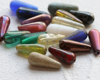 May include: Assortment of colorful glass teardrop beads with iridescent and metallic finishes. The beads are various shades of blue, green, red, gold, and brown.