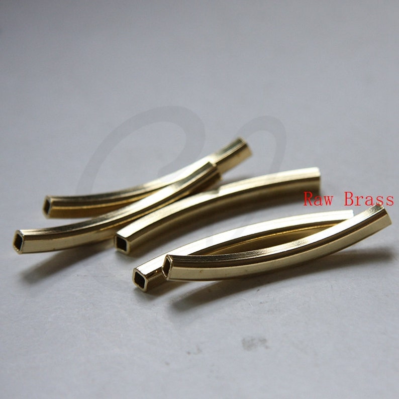Puede incluir: Cuatro barras de metal de color dorado con bordes redondeados y extremos cuadrados. Las barras est&aacute;n curvadas y dispuestas en forma de cruz. El texto "Raw Brass" es visible en la imagen.