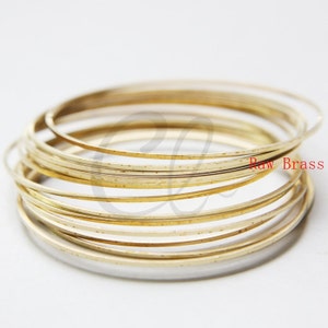 May include: A stack of 10 thin, round, gold-colored brass wire rings. The rings are stacked on top of each other, with the top ring slightly offset from the bottom ring. The rings are all the same size and have a smooth, polished finish. The text "Raw Brass" is visible in the image.