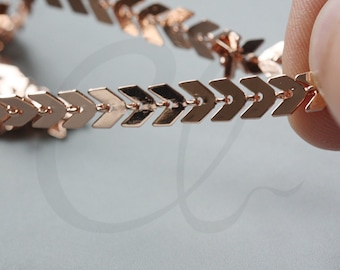 May include: A rose gold chain necklace with arrow-shaped links. The chain is delicate and has a modern look.