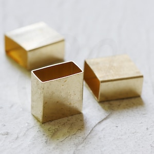 May include: Three gold-colored metal square-shaped boxes with open tops. The boxes are made of a shiny metal and have a slightly textured surface.