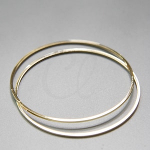 Puede incluir: Dos aros de metal dorado, uno ligeramente más grande que el otro, están apilados uno encima del otro. Los aros son simples y elegantes.