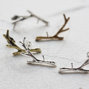 May include: Silver and gold twig earrings. The earrings are in the shape of a small branch with a few offshoots. The earrings are a simple and elegant design.
