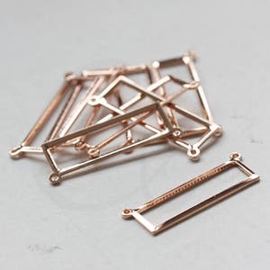 Op de afbeelding: Een groep rechthoekige frames van roosgoudkleurig metaal met afgeronde hoeken. De frames hebben kleine gaatjes in elke hoek.