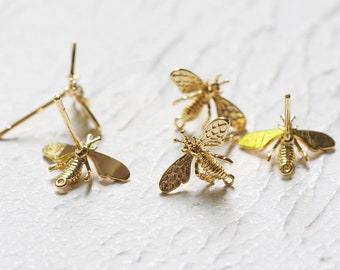 May include: Four gold bee charms with earring posts. The bees have detailed wings and bodies.
