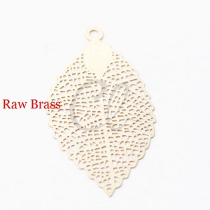 May include: A delicate, filigree leaf charm made of raw brass. The leaf has a detailed, intricate design with a hole at the top for hanging.