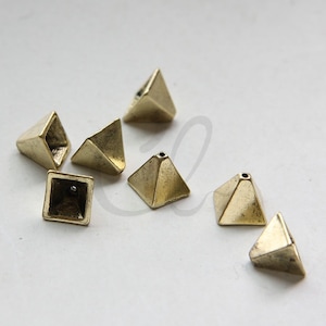 May include: Eight gold-toned pyramid-shaped metal beads with a hole in the top. The beads are scattered on a white surface.