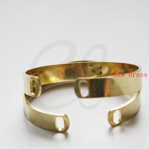 May include: A gold-toned metal bracelet with two open loops on each end. The bracelet is made of raw brass.