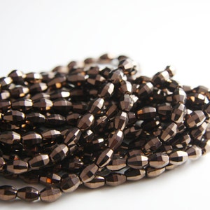 May include: A strand of brown faceted glass beads. The beads are oval shaped and have a metallic sheen.