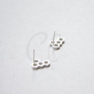 May include: A pair of silver honeycomb stud earrings. The earrings are made of a metal that resembles silver and have a honeycomb pattern.