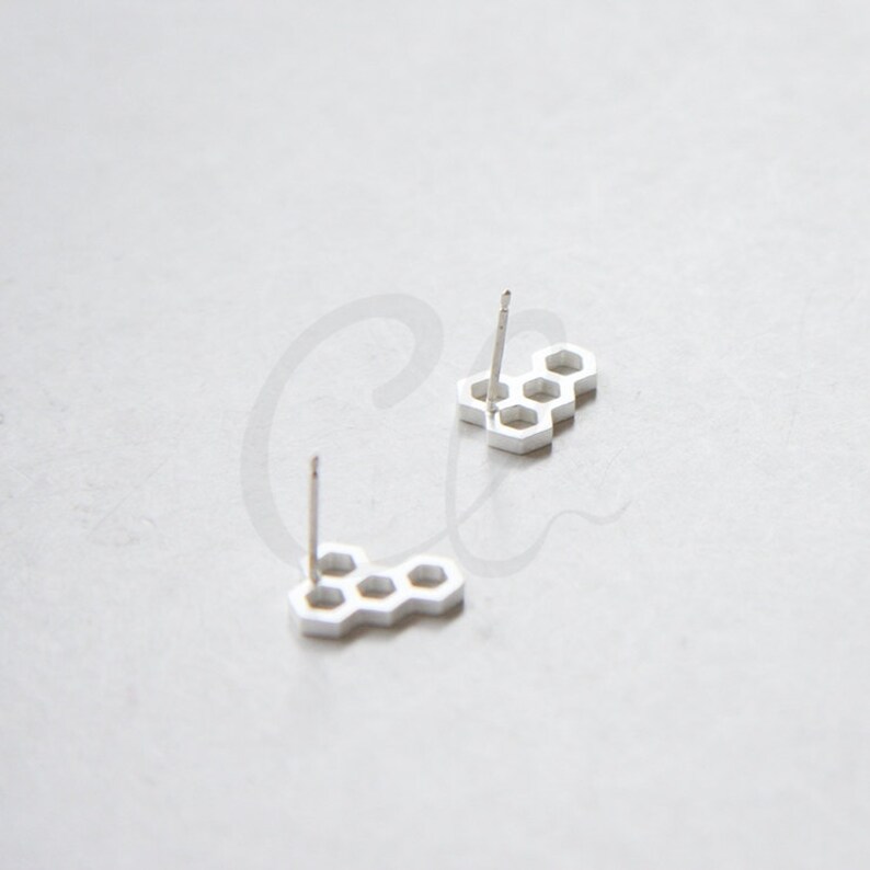 May include: A pair of silver honeycomb stud earrings. The earrings are made of a metal that resembles silver and have a honeycomb pattern.