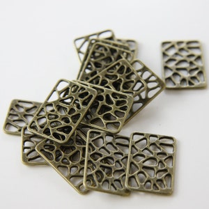 May include: A pile of antique gold metal charms with a geometric, lattice design. The charms are rectangular and have a delicate, intricate pattern.