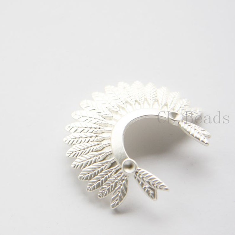 May include: Silver feather headdress charm for jewellery making. The charm is shaped like a headdress with feathers on the sides. It is a great addition to necklaces, bracelets and earrings.