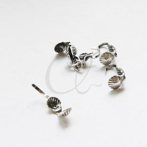 May include: Silver-toned metal shell-shaped clasps for jewelry making. The clasps have a hook on one side and a shell on the other. There are five clasps in total.
