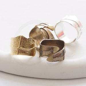 May include: Four different textured metal rings. The rings are all different shapes and sizes. The rings are made of gold, silver, and bronze.