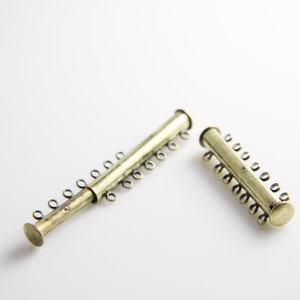 Puede incluir: Dos piezas de conexión de metal dorado para la elaboración de joyas. Cada pieza tiene una serie de pequeños bucles a lo largo de la longitud del tubo.