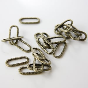 May include: A pile of antique gold-toned metal oval-shaped rings with a decorative patterned edge. The rings are about 1 inch in diameter.