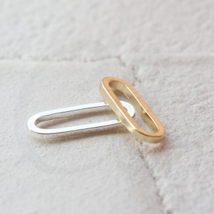Op de afbeelding: Twee ovale ringen, een zilveren en een gouden, zijn in elkaar gehaakt. De ringen zijn glad en hebben een gepolijste afwerking.