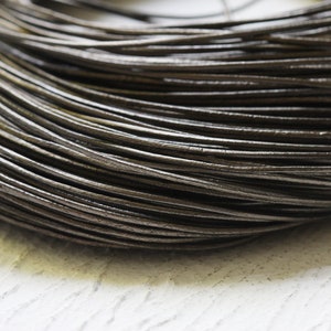 May include: Close-up of a reel of dark brown leather cord. The cord is smooth and supple, and it is ideal for crafting jewellery, bracelets, and other leather goods.