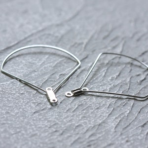 May include: Two silver metal hoops with a rounded and a more angular shape. The hoops are connected by a small metal bar.