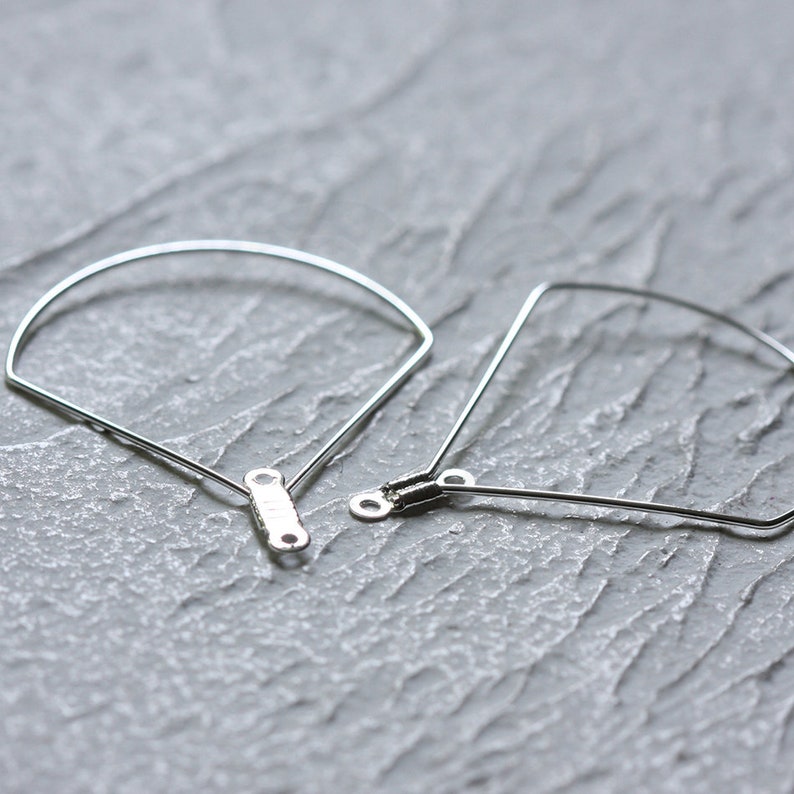 May include: Two silver metal hoops with a rounded and a more angular shape. The hoops are connected by a small metal bar.