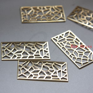 May include: Five gold-coloured metal rectangular frames with a geometric pattern cut out. The frames are on a grey surface. "Raw Brass" is written in red on the surface.