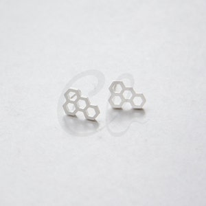 May include: A pair of silver honeycomb stud earrings. The earrings are small and delicate, and they have a simple, modern design.