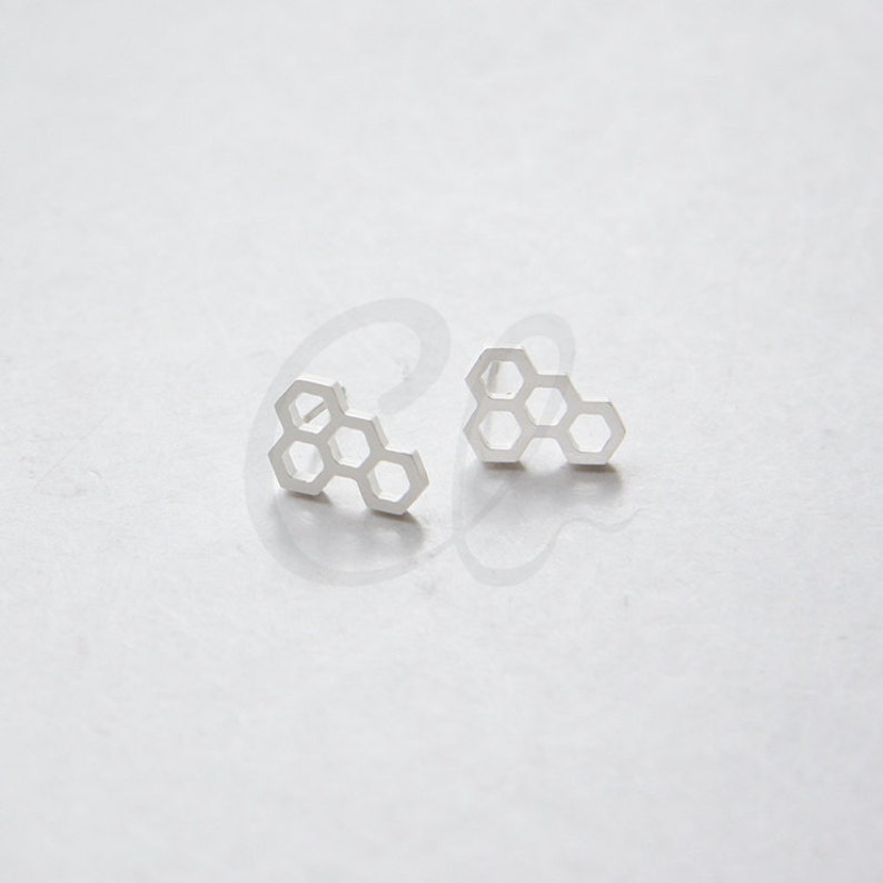 May include: A pair of silver honeycomb stud earrings. The earrings are small and delicate, and they have a simple, modern design.