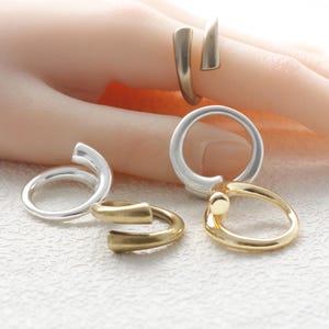 May include: Five different silver and gold rings. The rings are all simple and modern in design. Some of the rings are open and some are closed.