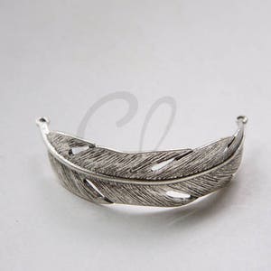May include: Silver feather shaped hair clip. The clip is open at the top and bottom, with a detailed feather design.