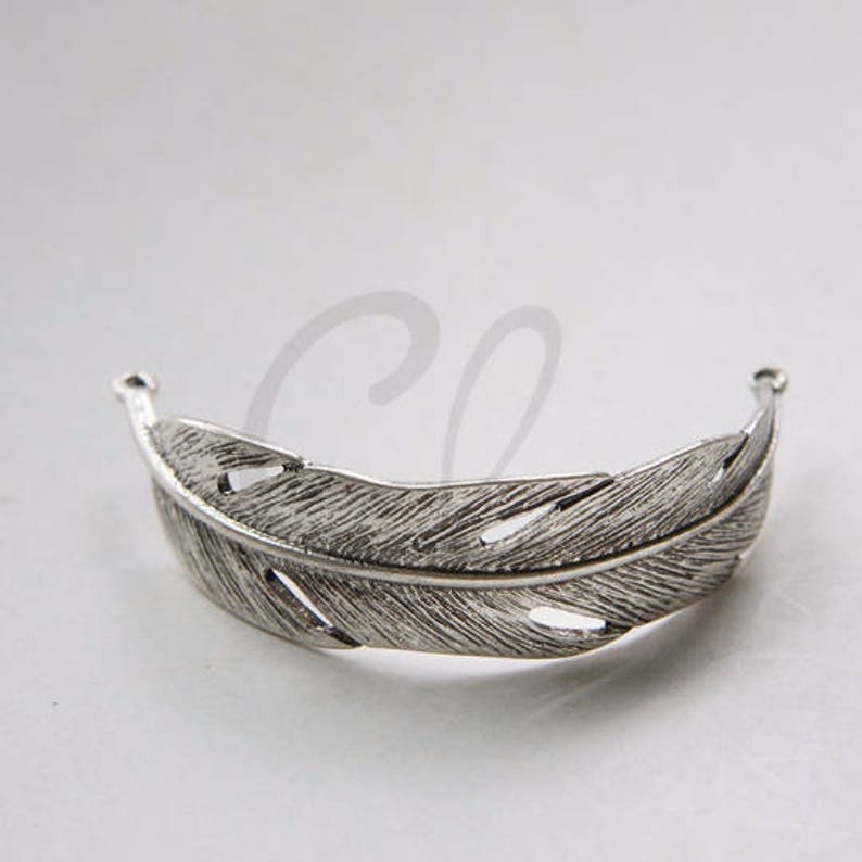 May include: Silver feather shaped hair clip. The clip is open at the top and bottom, with a detailed feather design.